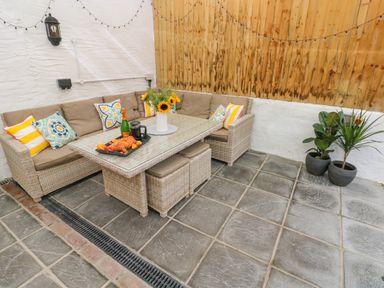 An outdoor seating area with a wicker sofa with cushions a glass table with croissants and flowers and two potted plants at Y Beudy in Crosswell Eglwyswrw near Newport Pembrokeshire