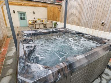 An outdoor hot tub with bubbling water next to a patio area with a wicker sofa set and table at Y Beudy in Crosswell Eglwyswrw near Newport Pembrokeshire