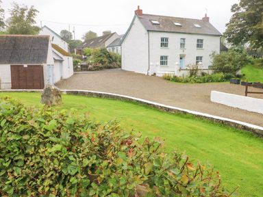 A white two-story house with blue windows and door surrounded by gravel driveway and green lawn at Y Beudy in Crosswell Eglwyswrw near Newport Pembrokeshire