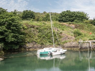 A small sailboat and motorboat on calm water near a green hillside with trees and rocks at Monarfon in Amlwch