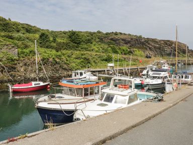 A small harbor with boats docked along a concrete quay and greenery on the hillside behind at Monarfon in Amlwch