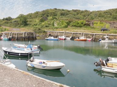 Small motorboats moored in a calm harbor with a stone wall and green hills in the background at Monarfon in Amlwch