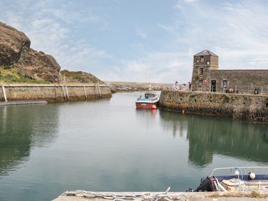 A small harbor with boats docked near stone walls and an old stone building at Monarfon in Amlwch