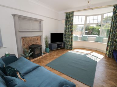 A living room with a fireplace a television and a bay window with cushions at Monarfon in Amlwch