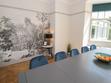 A dining room with blue chairs a grey table a window and a black and white forest mural at Monarfon in Amlwch