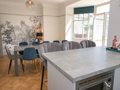 A dining room with grey and blue chairs around a table and a grey countertop with bar stools at Monarfon in Amlwch