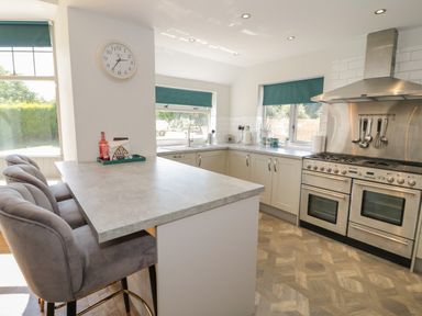 A kitchen with a stove and ovens a counter with bar stools and windows with green blinds at Monarfon in Amlwch