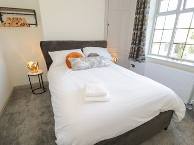 A bedroom with a double bed white bedding and pillows next to a window with curtains at Monarfon in Amlwch