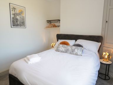 A bedroom with a bed with white bedding and pillows with a small table holding a lamp and a wall shelf with hangers at Monarfon in Amlwch