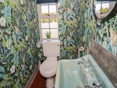 A small bathroom with toilet sink and window with plant on toilet tank surrounded by floral and leaf patterned wallpaper at Monarfon in Amlwch