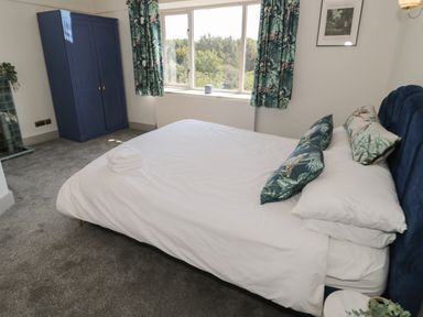 A bedroom with a bed white bedding blue pillows a blue wardrobe and a window with patterned curtains at Monarfon in Amlwch