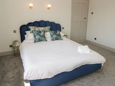 A bedroom with a blue upholstered bed with white bedding and patterned cushions at Monarfon in Amlwch