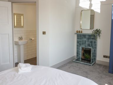 A bedroom with a bed and folded towels near a tiled fireplace with a mirror and a door leading to a bathroom at Monarfon in Amlwch