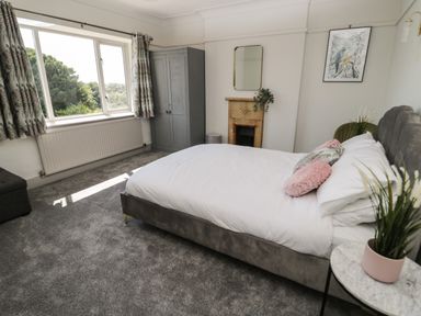 A bedroom with a bed pillows and plants next to a window and wardrobe at Monarfon in Amlwch