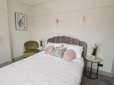 A bedroom with a bed and cushions two side tables with plants a green chair and a framed picture at Monarfon in Amlwch