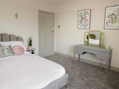 A bedroom with a bed with pillows a nightstand with a plant a dressing table with a mirror and wall art at Monarfon in Amlwch
