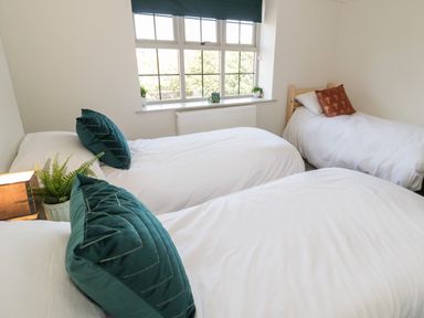 A bedroom with three single beds white bedding green and brown pillows a window and plants at Monarfon in Amlwch