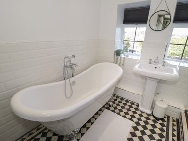 A bathroom with a freestanding bathtub sink a round mirror and checkered floor at Monarfon in Amlwch