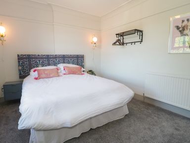 A bedroom with a double bed white bedding pink pillows wall lights and a wall mounted shelf with hangers at Monarfon in Amlwch