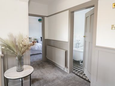 A hallway with a small round table and vase with dried flowers and two open doors showing a bedroom and bathroom at Monarfon in Amlwch
