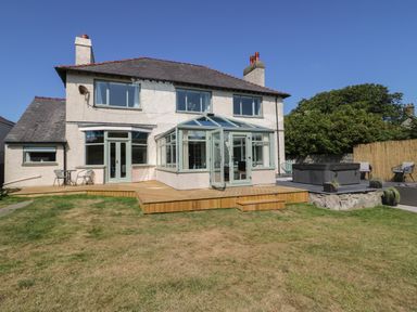 A backyard with a wooden deck patio attached to a two-story house with a glass conservatory and outdoor seating at Monarfon in Amlwch