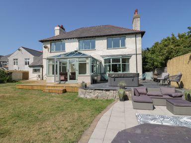 The backyard of a two-story house with a conservatory deck seating area and hot tub at Monarfon in Amlwch