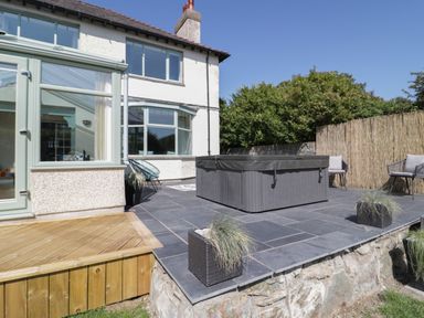 An outdoor patio with a covered hot tub two chairs and potted plants at Monarfon in Amlwch