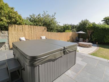 An outdoor patio area with a covered hot tub chairs umbrella and fire pit at Monarfon in Amlwch