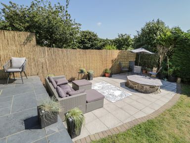 An outdoor patio with seating furniture a fire pit umbrella and plants at Monarfon in Amlwch