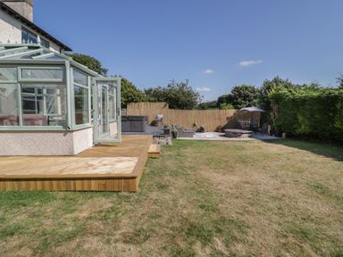 A backyard with a wooden deck and a conservatory attached to a house and outdoor seating areas at Monarfon in Amlwch