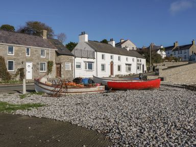 Fishing boats on a pebble beach in front of stone and white houses at Monarfon in Amlwch