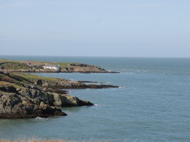 Rocky coastline with a white house near the shore and sea in the background at Monarfon in Amlwch