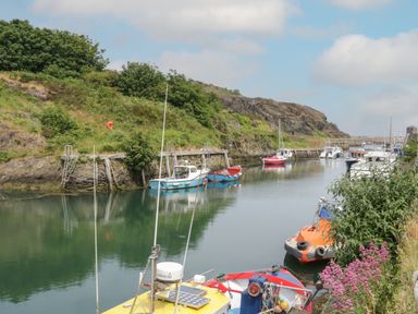 A small harbor with boats docked along the water and greenery on the surrounding hills at Monarfon in Amlwch