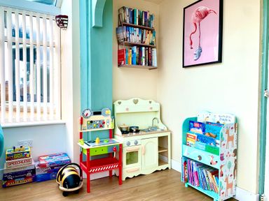 A children's play area with toy kitchen, bookshelf filled with books, toy tools and board games at Monarfon in Amlwch