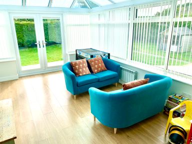 A conservatory with two blue sofas and decorative pillows a foosball table and board games next to a yellow chair at Monarfon in Amlwch