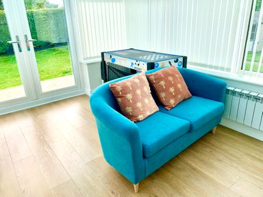 A blue sofa with two brown palm tree patterned cushions in a room with wooden floor next to glass doors and windows at Monarfon in Amlwch