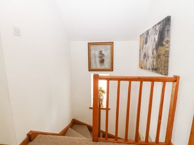 A stairway with wooden railing and framed paintings on the walls at Ty Gwennol in Llanfaethlu