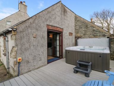 An outdoor deck area with a hot tub steps and an open door to a stone and stucco house at Ty Gwennol in Llanfaethlu