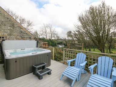 An outdoor deck with a hot tub and two blue chairs overlooking a garden at Ty Gwennol in Llanfaethlu