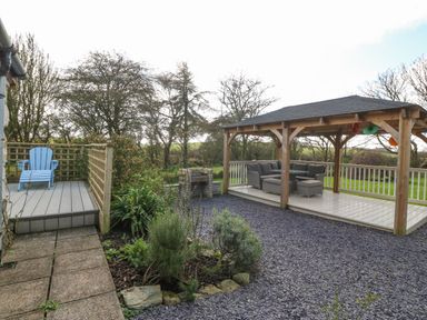 An outdoor seating area with a blue chair on a deck and a covered patio with a sofa set at Ty Gwennol in Llanfaethlu
