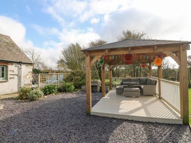 An outdoor wooden gazebo with seating and decorations next to a house at Ty Gwennol in Llanfaethlu