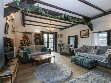 A living room featuring a sofa, armchairs, and a Christmas tree at Ty Gwennol in Llanfaethlu