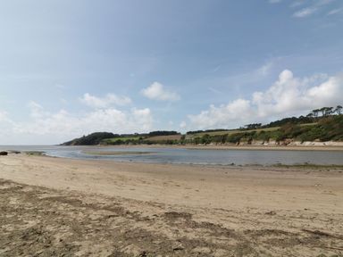 A sandy beach with water and distant green hills under a partly cloudy sky at 3 Rock Cottages in Kingston