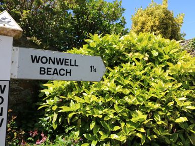 A signpost pointing to Wonwell Beach surrounded by green bushes under a blue sky at 3 Rock Cottages in Kingston