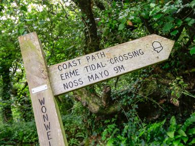 A wooden signpost in a wooded area pointing to coast path erme tidal crossing noss mayo nine meters at 3 Rock Cottages in Kingston