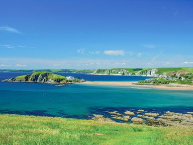 A coastal landscape with green cliffs sandy beach and blue ocean at 3 Rock Cottages in Kingston