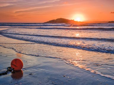 A beach with waves and an orange buoy on the wet sand at sunset at 3 Rock Cottages Kingston