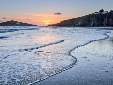 A beach with waves coming to shore and cliffs in the background at sunset at 3 Rock Cottages in Kingston