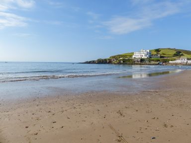 A sandy beach with gentle waves and buildings on a hill in the background at 3 Rock Cottages in Kingston
