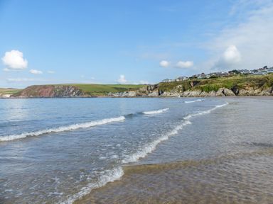 A beach with gentle waves and rocky cliffs with houses on top at 3 Rock Cottages in Kingston